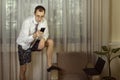 Young man in a white shirt with a tie and underwear works at home and conducts a video conference via smartphone. Royalty Free Stock Photo