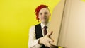 Young man in white shirt, vest and tie with cardboard box on yellow background in studio. Male courier with package