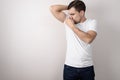 Young guy in white t-shirt clamps his nose from smell of sweat from his armpits on gray background with copy space Royalty Free Stock Photo