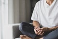 Young man in a white t-shirt and grey pants sat on the sofa practicing meditation, sitting in a lotus pose alone in the morning at Royalty Free Stock Photo