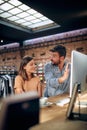 Blurred faces of young man and woman colleagues talking in front of table with desktop computer, in clothing store Royalty Free Stock Photo