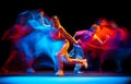 Young man and woman dancing hip-hop in sportive style clothes on dark background at dance hall in mixed neon light Royalty Free Stock Photo