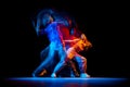 Young man and woman dancing hip-hop in sportive style clothes on dark background at dance hall in mixed neon light Royalty Free Stock Photo