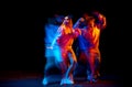 Young man and woman dancing hip-hop in sportive style clothes on dark background at dance hall in mixed neon light Royalty Free Stock Photo