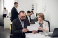 Young man and woman discuss something, colleages are busy with work beside them in the office