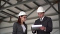 Young man and woman in helmets with documents at a construction site. Businessmen in suits conclude an agreement. A man