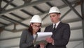 Young man and woman in helmets with documents at a construction site. Businessmen in suits conclude an agreement. A