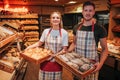 Young man and woman hold baskets of fresh tasty white dark bread in hands. They look on camera pose and smile. Positive Royalty Free Stock Photo