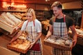 Young man and woman hold baskets of fresh tasty white dark bread in hands. Working in bakery or grocery store. Busy Royalty Free Stock Photo