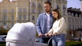Young man and woman looking at baby swinging carriage, family love, hugging