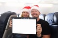 Young man and woman in santa claus hats holding digital tablet in cabin of airplane Royalty Free Stock Photo