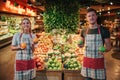 Young man and woman stand at fruit boxes in grocery store. She hold oranges while he get green apples in hands. Posing