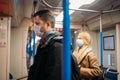 Young man and woman standing near handrails in subway car.