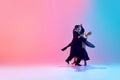 Young man and woman, talented ballroom dancers in motion, dancing in black costumes against gradient pink blue Royalty Free Stock Photo