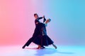 Young man and woman, talented ballroom dancers in motion, dancing in black costumes against gradient pink blue Royalty Free Stock Photo