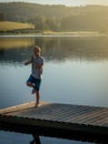 Young man on wooden pontoon or pier practicing yoga & relaxing with reflection in water .on holiday