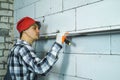 Young man in work wear checking straightness of block wall with bubble level