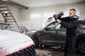 Young man worker cleaning modern red car hood with foam and pressurized water at service station