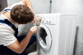 Young man worker in uniform repairing washing machine at home in the toilette professional repair service Royalty Free Stock Photo