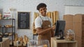 Young man working in a bakery shop, smiling while using a computer with bread and pastries in the background Royalty Free Stock Photo