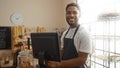 Young man working in a bakery smiling at the camera standing behind the counter with shelves of bread and sweets in the background Royalty Free Stock Photo