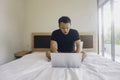 Young man working from the bed, pondering while looking at his laptop Royalty Free Stock Photo