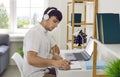 Young man working in his home office, sitting at desk, using laptop and writing in notebook Royalty Free Stock Photo