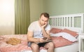 Young man working from home in bedroom, feelling bored and tired holding a phone and laptop in his arms Royalty Free Stock Photo