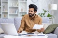 Young man working at home with documents and papers, homework, paying bills and loans, hispanic sitting on sofa in Royalty Free Stock Photo