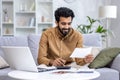 Young man working at home with documents and papers, homework, paying bills and loans, hispanic sitting on sofa in Royalty Free Stock Photo