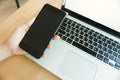 Young man working from home using smart phone mockup and laptop computer, man`s hands using smart phone in interior. Royalty Free Stock Photo