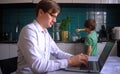 Young man working in the kitchen at a laptop. Father with son. Home office with kids. Royalty Free Stock Photo