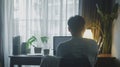 A young man working on a laptop facing the window, view from his back. Work from home concept, home office. Generative ai Royalty Free Stock Photo