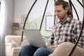 Young man working with laptop on hanging armchair