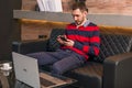 Man working on a laptop at his desk in the office sitting on a sofa and holding a phone Royalty Free Stock Photo