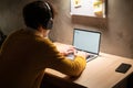 Young man working on laptop in home office. Male student studying in university dormitory at night, typing on laptop