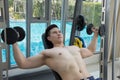 Young Man Working Out Shoulders with dumbbells, training in gym