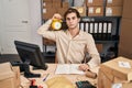 Young man working at small business ecommerce holding alarm clock thinking attitude and sober expression looking self confident Royalty Free Stock Photo