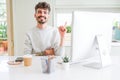 Young man working using computer with a big smile on face, pointing with hand and finger to the side looking at the camera Royalty Free Stock Photo