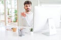 Young man working using computer pointing with finger to the camera and to you, hand sign, positive and confident gesture from the Royalty Free Stock Photo