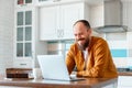 Young man working using laptop in kitchen in home interior. Smiling Freelancer works remotely from home. Happy man owner Royalty Free Stock Photo