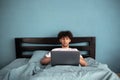 Young man working using laptop lying in bed in the morning, overtime remote work on weekend, freelancer working at home Royalty Free Stock Photo