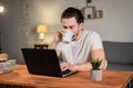 A young man works from home and drink tea at desk with computer. Bad idea. Liquid in cup, coffee Royalty Free Stock Photo