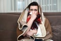 Young man wrapped in plaid sitting on the sofa bowing nose with handkerchief looking sick illness at home