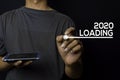 Young man write on 2020 Loading text with smartphone isolated on black background Royalty Free Stock Photo