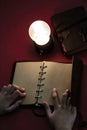 Young man writing on a blank page of a vintage leather book under the low light condition with a yellow, light bulb Royalty Free Stock Photo