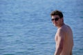 A young man 25-30 years old European appearance on the beach against the background of the sea  looks into the lens  smiles  naked Royalty Free Stock Photo