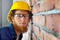 Young man in a yellow helmet looks at the brick wall