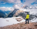 Young man in yellow jacket on the hill and snowy mountains