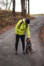 young man in a yellow jacket scratches behind the ear of a Cesky fousek a hunting dog that sits obediently next to his leg.